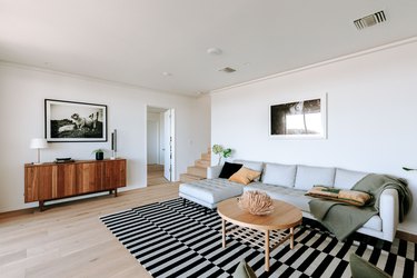 Living room with light wood floor, wood sideboard, black-white striped rug, gray sofa, and light wood round coffee table
